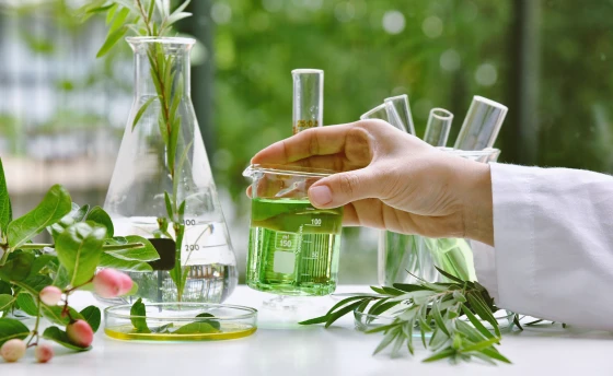 Un científico con bata de laboratorio sostiene un vaso que contiene un líquido verde.